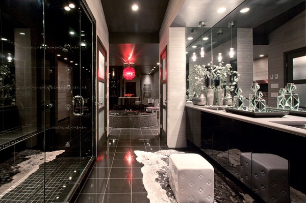Bogato zdobiona łazienka, utrzymana w luksusowym stylu, pełnym przepychu, z licznymi przeszkleniami, elementami połyskującymi, dużymi lustrami łazienkowymi, licznymi podświetleniami ledowymi, ciemnymi płytkami podłogowymi oraz jasnymi akcentami ścian.